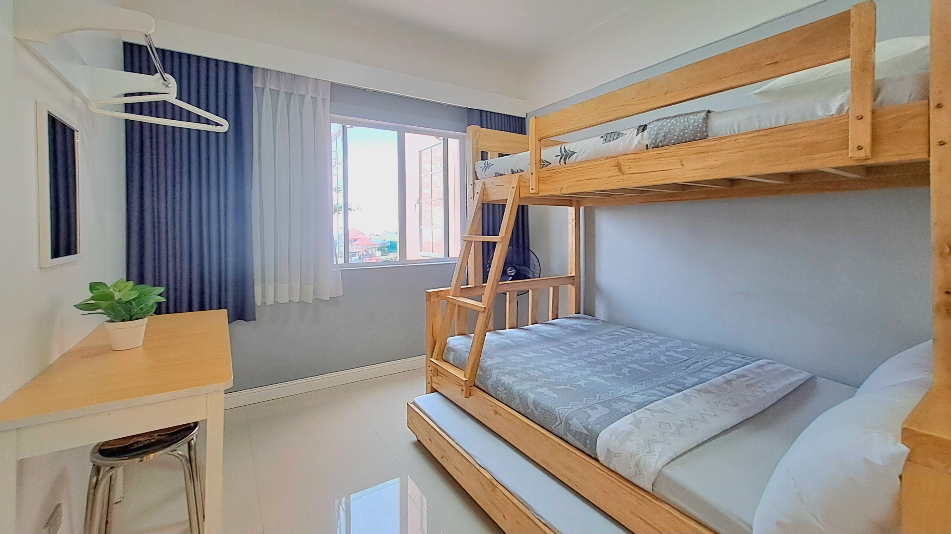 Een slaapkamer met een stapelbed, een bureau, een hanglamp en een raam met gordijnen.