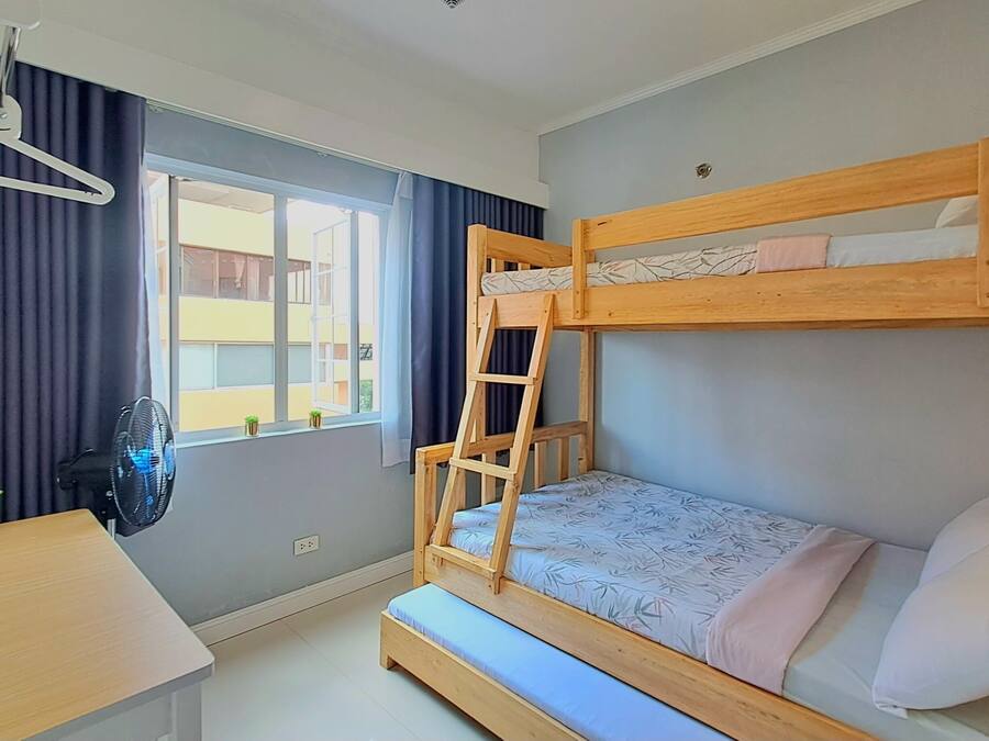 Une petite pièce comprenant un lit superposé, un bureau, une chaise, une petite plante et une fenêtre avec des rideaux.