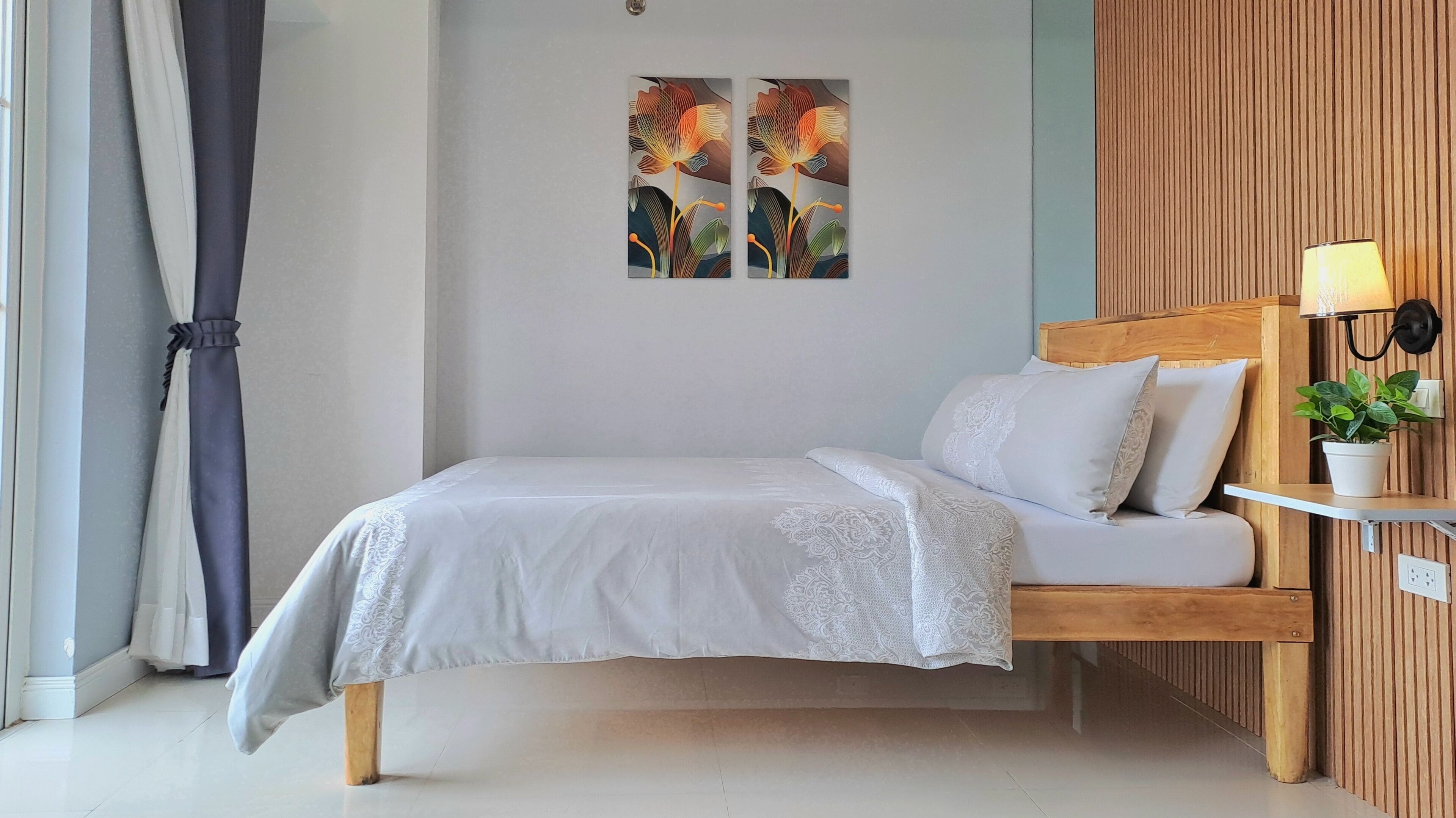 A bedroom with a wooden bed frame, white bedding, a bedside lamp, and a potted plant.