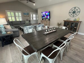 Un coin repas avec une table en bois foncé et des chaises blanches, un téléviseur fixé au mur et une boussole décorative accrochée au mur.