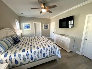 Une chambre à coucher comprenant un lit, un ventilateur de plafond, une commode et un téléviseur fixé au mur.