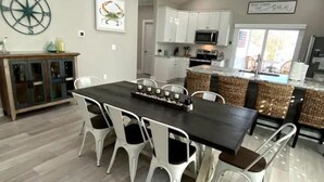 Een moderne keuken met witte kasten, een centraal eiland en een eethoek met een donker houten tafel en witte stoelen.