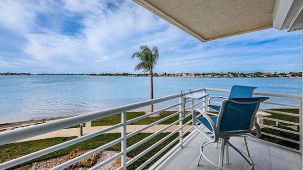 A balcony with a view of a calm body of water, a palm tree, and a distant shoreline. - Club Bahia Happiness Comes in (St. Petersburg)