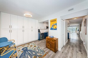 Une cuisine spacieuse avec des meubles blancs, un coin repas avec une chaise bleue et blanche, et un couloir menant à un balcon avec vue.