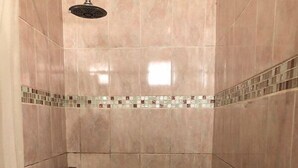 Une petite salle de douche carrelée, équipée d’un pommeau de douche et d’une poignée de porte.