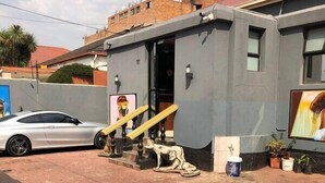 Un bâtiment à la façade grise, un escalier menant à une porte et une voiture garée.