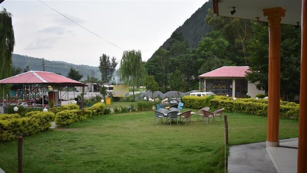 A grassy outdoor area with a red-roofed building, several chairs, and a small structure with a yellow sign. - Ever Green Hotel & Restaurant (Balakot)