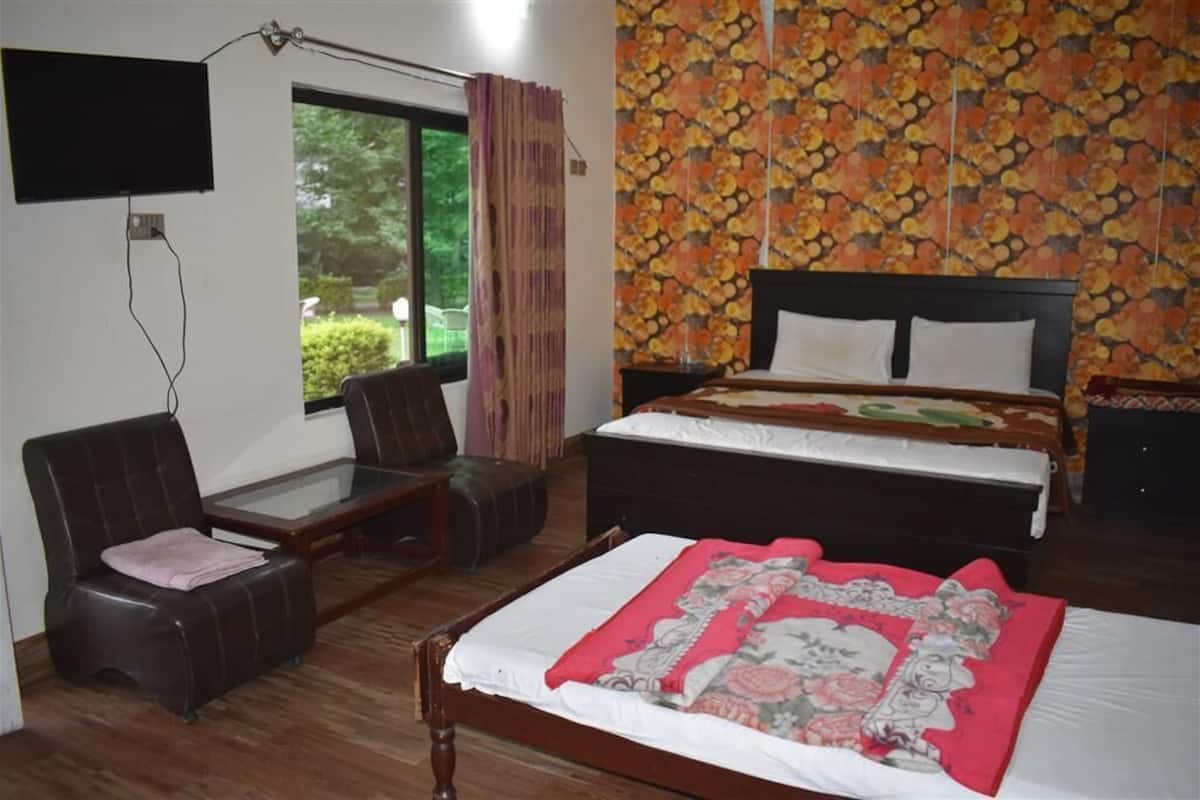A bedroom with a bed, a desk, a chair, a TV, and a window with curtains.