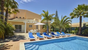 Una piscina con sillas de descanso, palmeras y un edificio con techo de tejas.