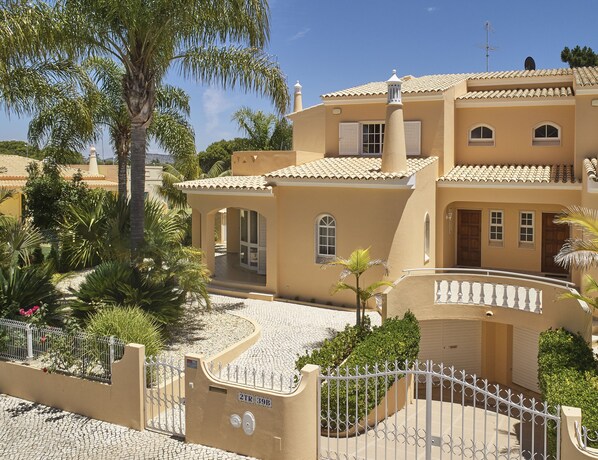 Um edifício de vários andares com fachada bege, entrada fechada por portão e caminho de pedras.