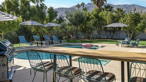 A pool area with lounge chairs, umbrellas, and a grill. - Palm Springs Artistic Pool Home – Walled Mid-Century Retreat with Pool, Spa & Mountain Views (Palm Springs)