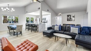 A spacious living area with a modern sofa, a dining table, and a kitchen in the background. - Palm Springs Artistic Pool Home – Walled Mid-Century Retreat with Pool, Spa & Mountain Views (Palm Springs)