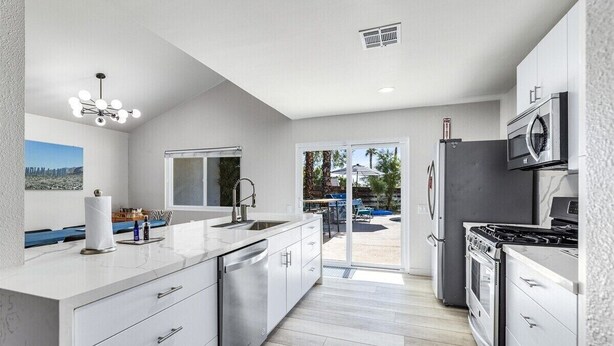 A modern kitchen with white cabinetry, stainless steel appliances, and a large window overlooking a patio area. - Palm Springs Artistic Pool Home – Walled Mid-Century Retreat with Pool, Spa & Mountain Views (Palm Springs)