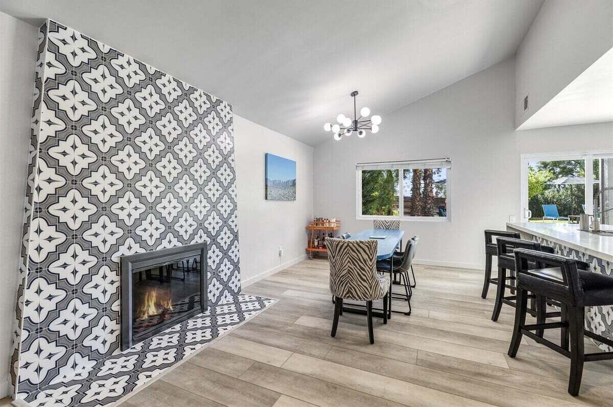 Une cuisine moderne avec un mur de crédence à motifs, une cheminée intégrée et un coin repas agrémenté de tabourets de bar.