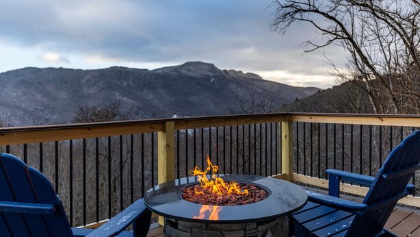 Une terrasse avec un foyer, deux chaises et une vue sur les montagnes.