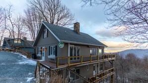Un chalet à deux étages doté d’un balcon et d’une cheminée en pierre.