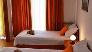 Ein Hotelzimmer mit zwei Betten, orangefarbenen Vorhängen, einer Nachttischlampe und einem Bild an der Wand.