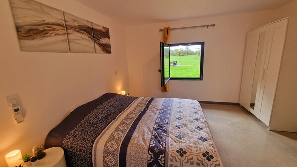 Relax in this serene bedroom with a large bed and a window overlooking a lush lawn.