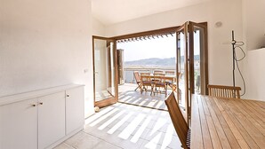 An open-plan living space with a balcony, wooden furniture, and a view of the mountains.