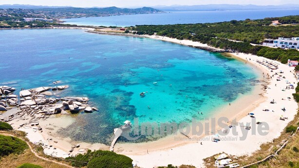 An aerial view of a coastal area with a beach, clear waters, and surrounding greenery.