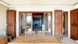 A spacious room with a wooden floor, a dining table with benches, and a kitchen area visible through an open door.