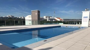 Een zwembad op het dak met helderblauw water, omgeven door betegelde vloeren en een glazen balustrade.