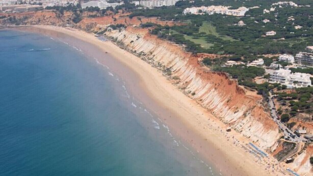 Luchtbeeld van een kustgebied met een zandstrand, kliffen en woongebouwen.