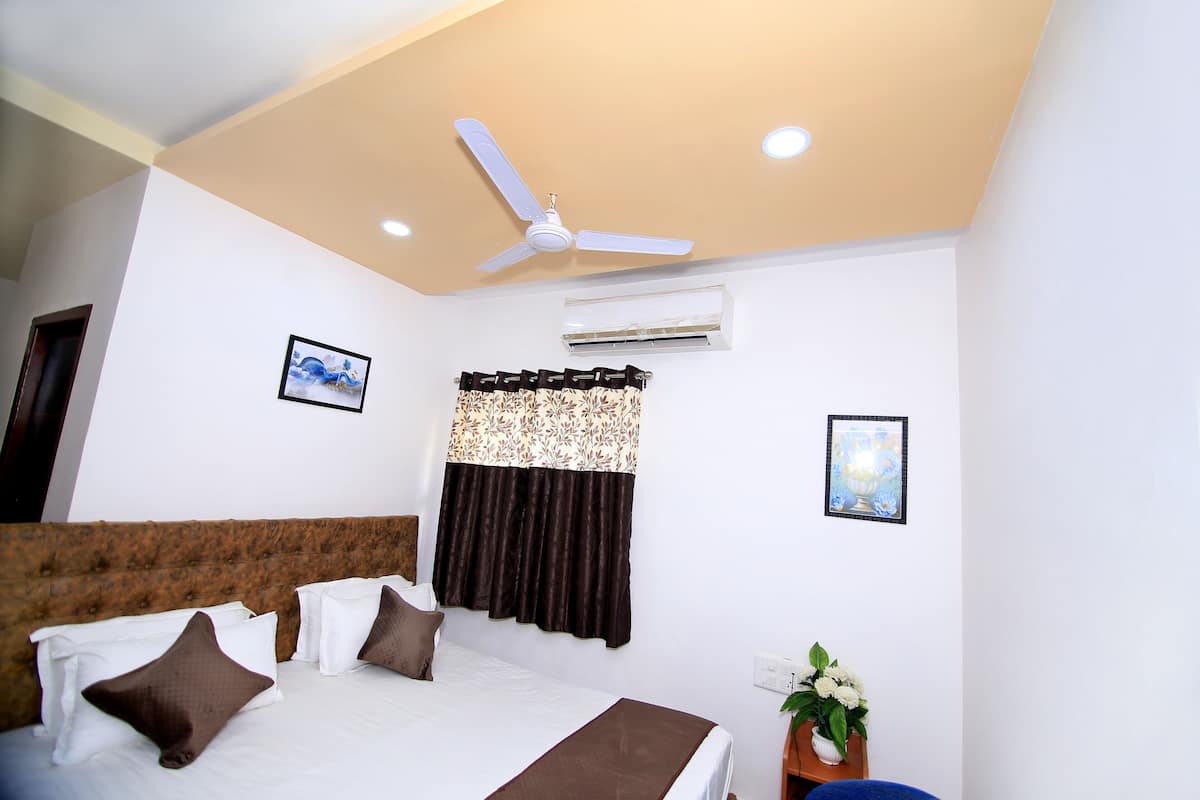 A hotel room with a bed, a ceiling fan, an air conditioning unit, and a window with curtains.