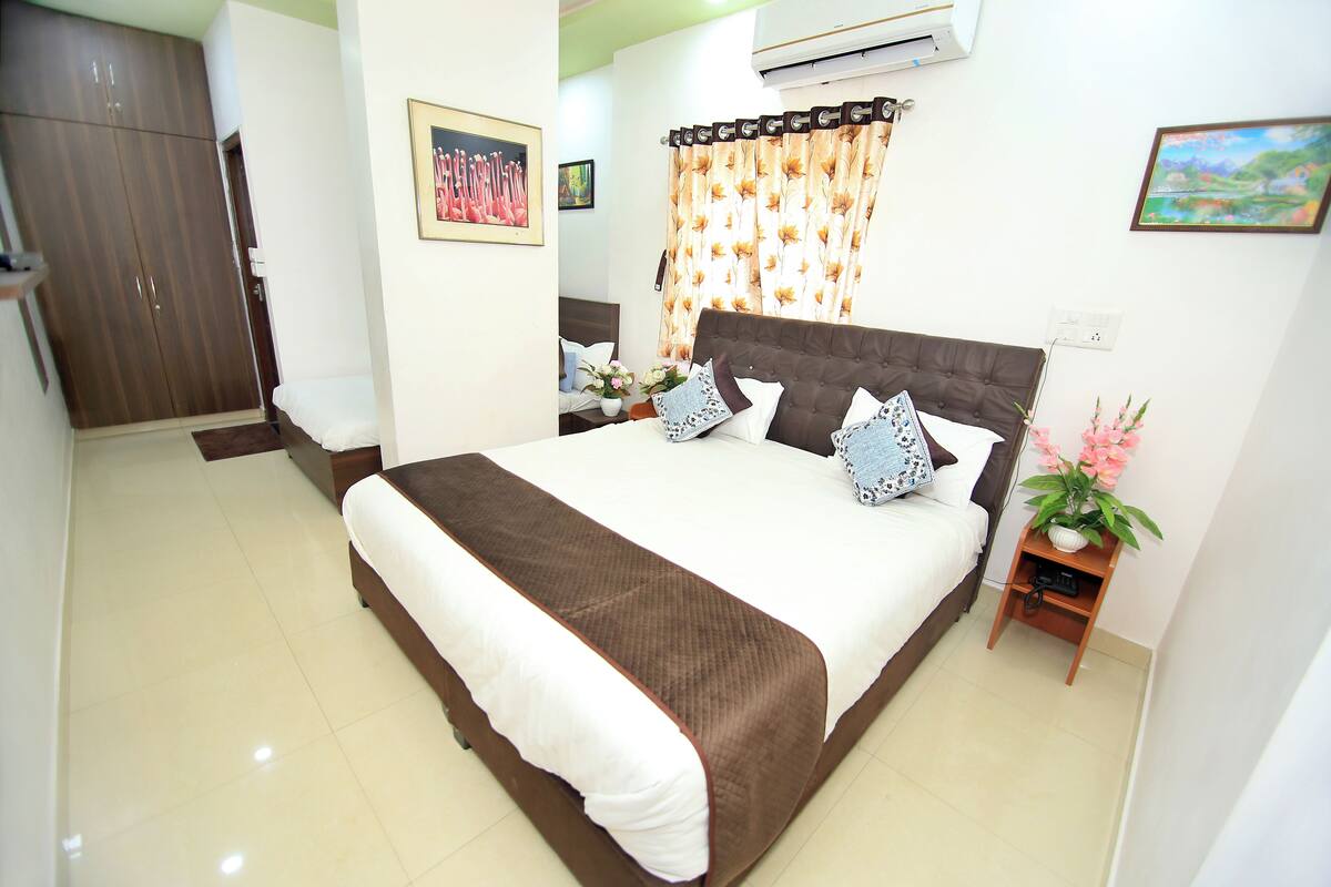 A neatly arranged bedroom with a large bed, a wardrobe, a nightstand with a plant, and a painting on the wall.