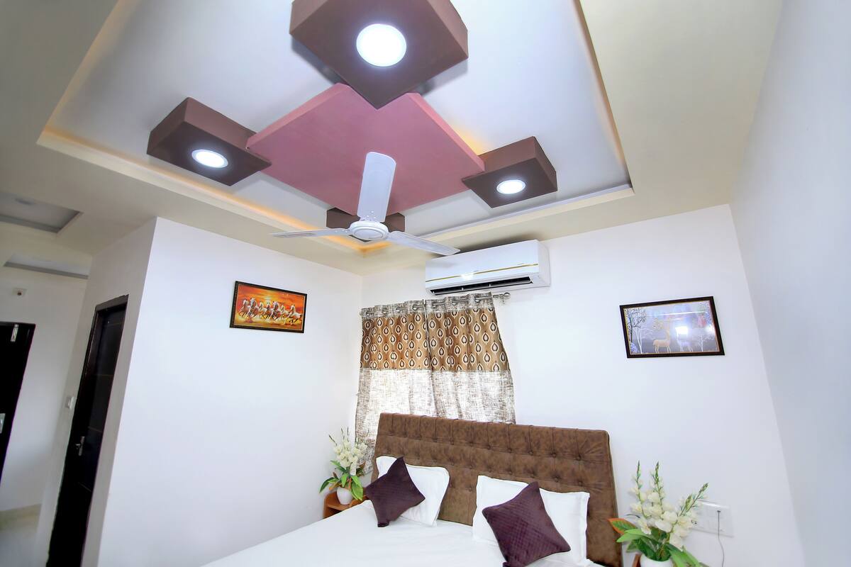 A bedroom with a bed, ceiling fan, air conditioning unit, and decorative wall elements.