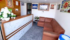 Et receptionsområde med en marmorreception, en brun lædersofa og et lille bord med blomster.
