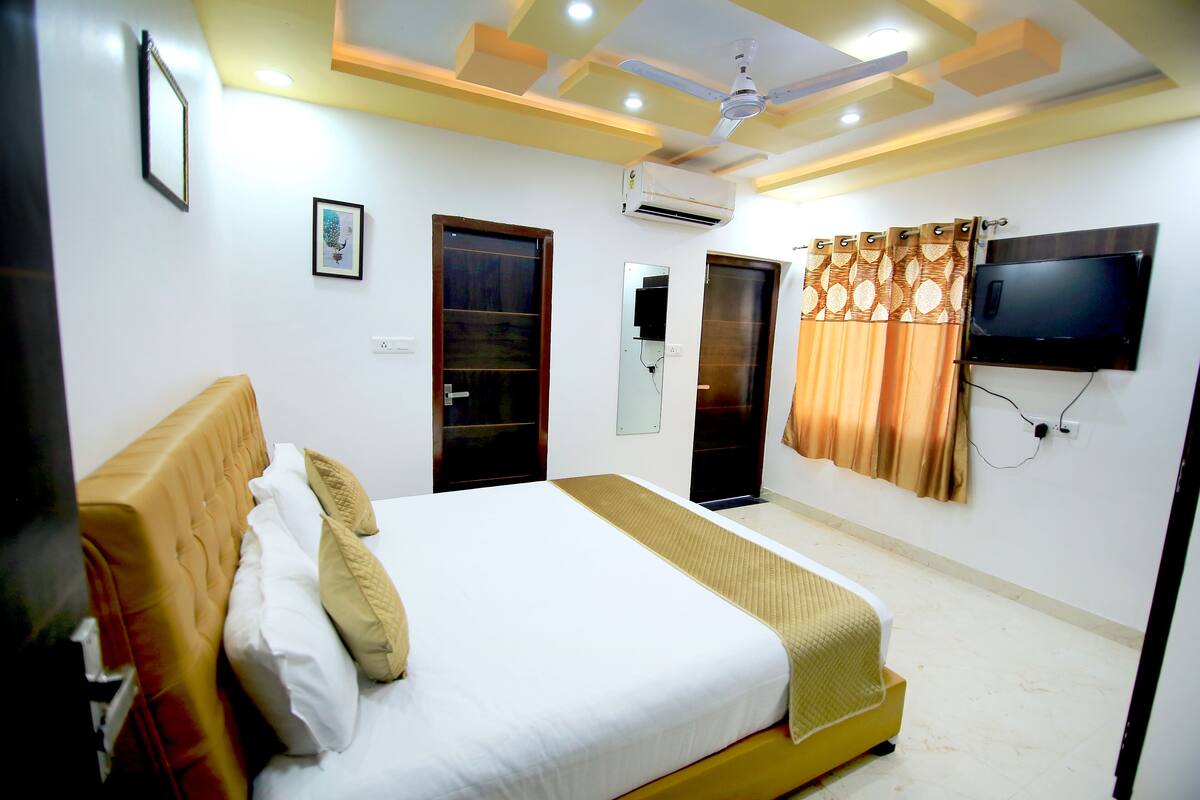 A hotel room with a bed, a television mounted on the wall, and an air conditioning unit.