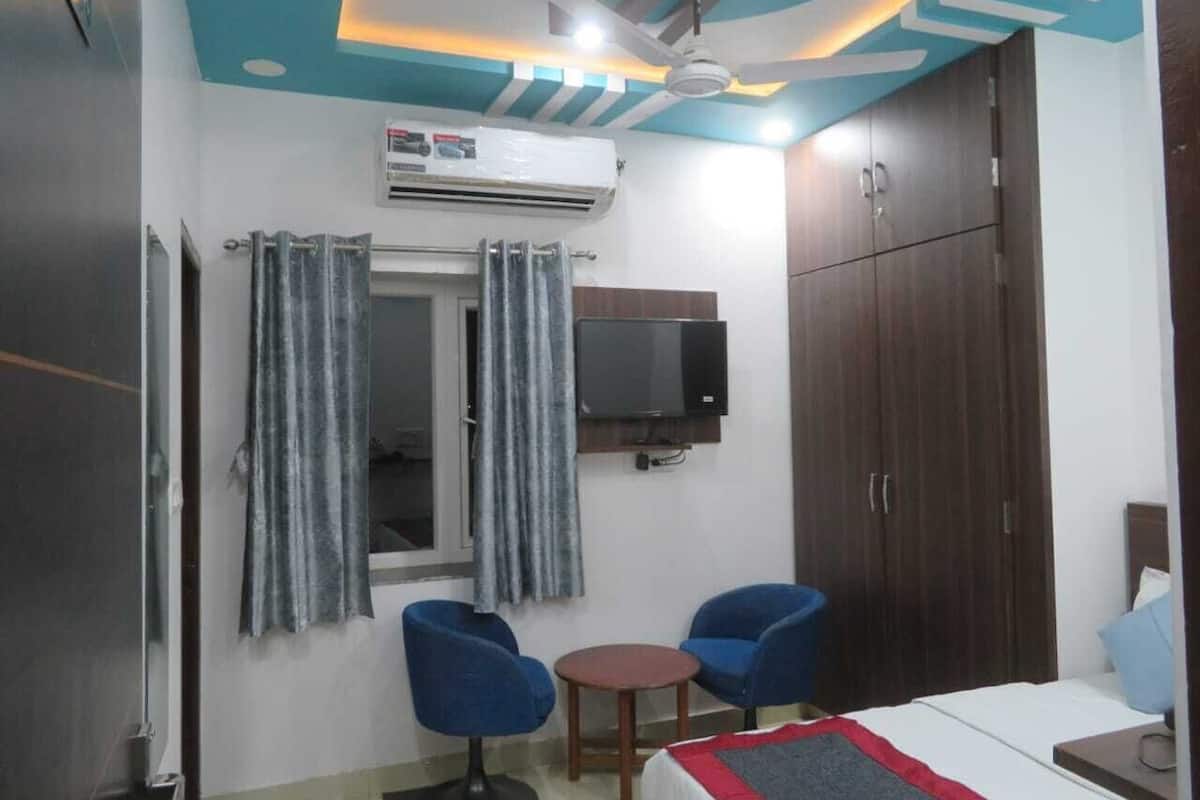 A hotel room with a bed, two chairs, a small table, a TV, and a wardrobe.