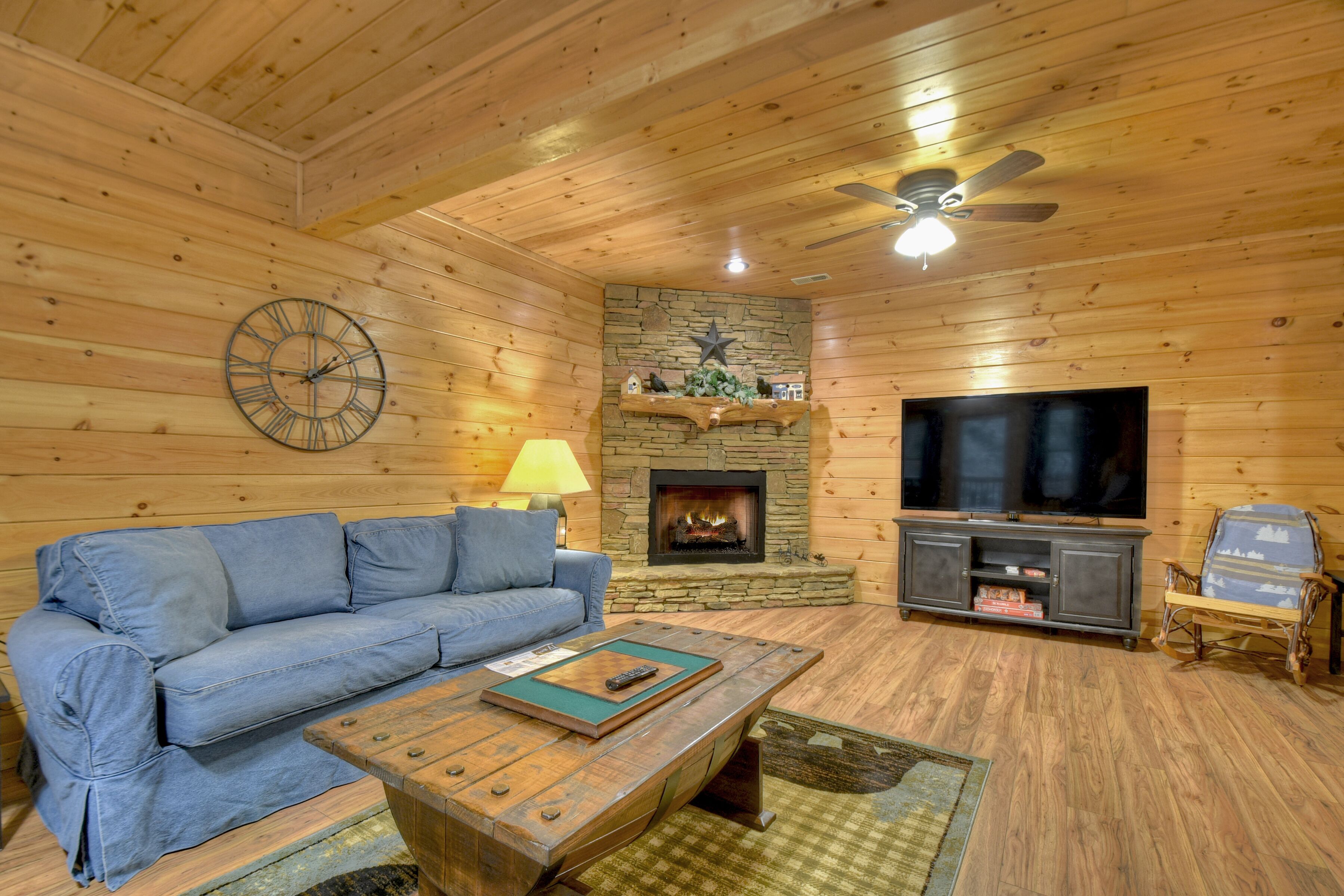 A cozy living room with a blue sofa, a wooden coffee table, a stone fireplace, and a television on a wooden stand.