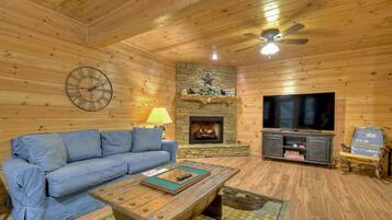 A cozy living room with a blue sofa, a wooden coffee table, a stone fireplace, and a television on a wooden stand.