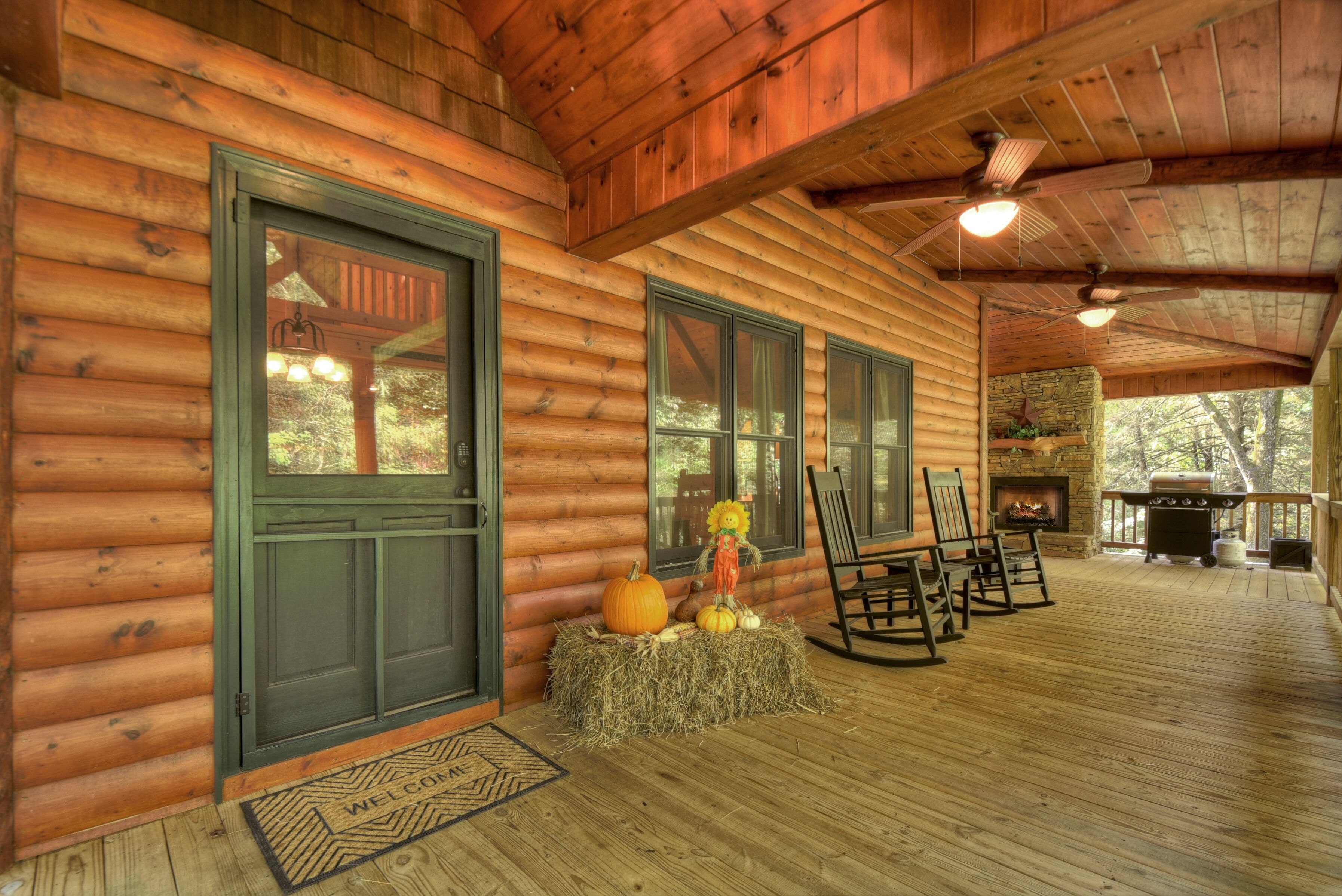 A log cabin with a fireplace, rocking chairs, and a hay bale decoration.