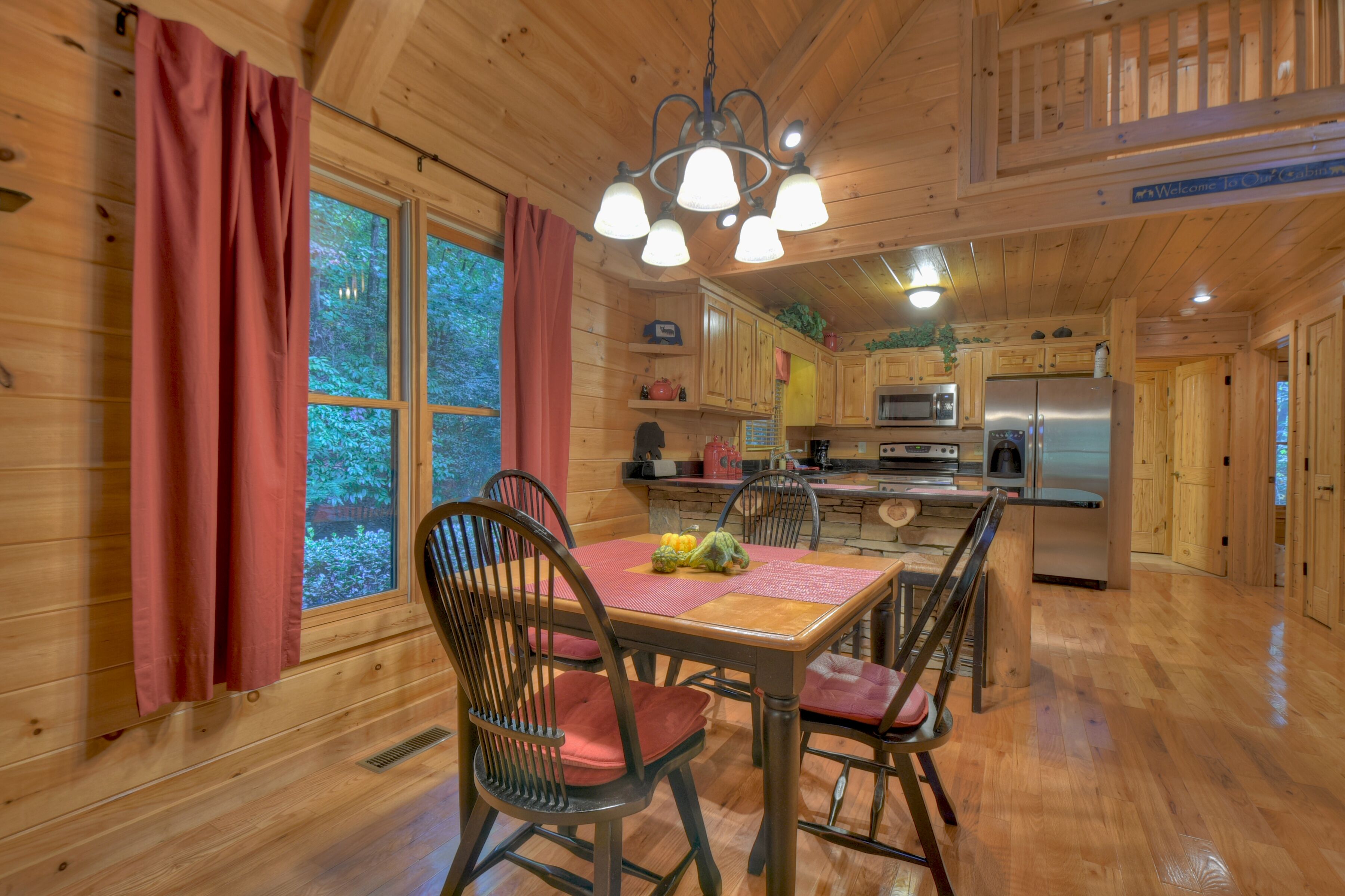 Interior de una cabaña de madera con una mesa de comedor, sillas, una zona de cocina y vistas al exterior.