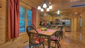 A wooden cabin interior with a dining table, chairs, a kitchen area, and a view of the outdoors. - Stoney Creek Retreat - Cherry Log, GA (Cherry Log)