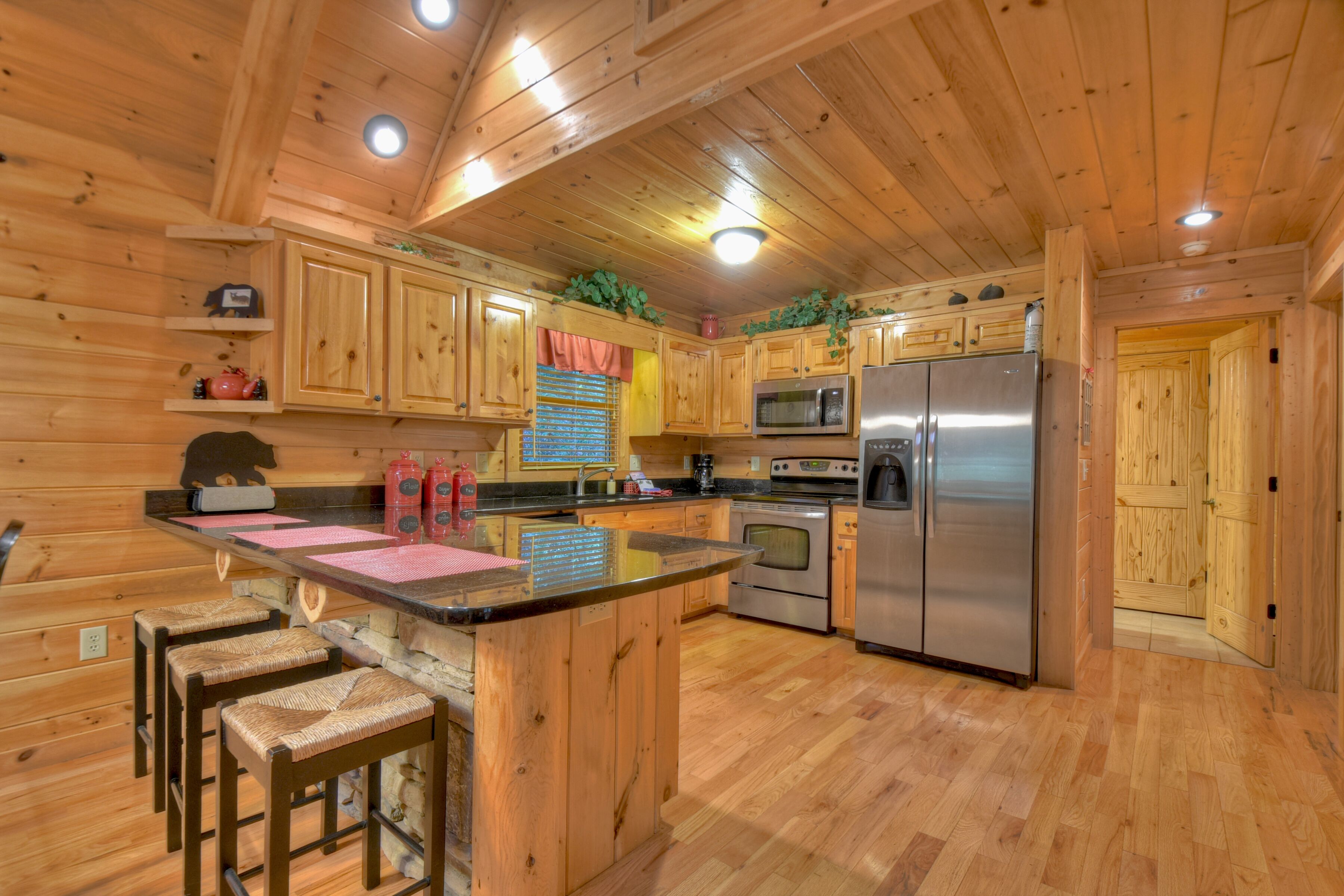 A wooden cabin interior with a kitchen featuring wooden cabinets, a stainless steel refrigerator, and a bar area with stools.
