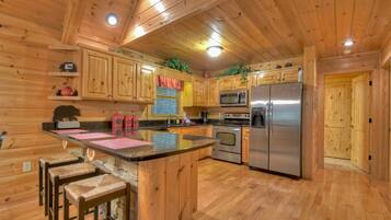 A wooden cabin interior with a kitchen featuring wooden cabinets, a stainless steel refrigerator, and a bar area with stools.