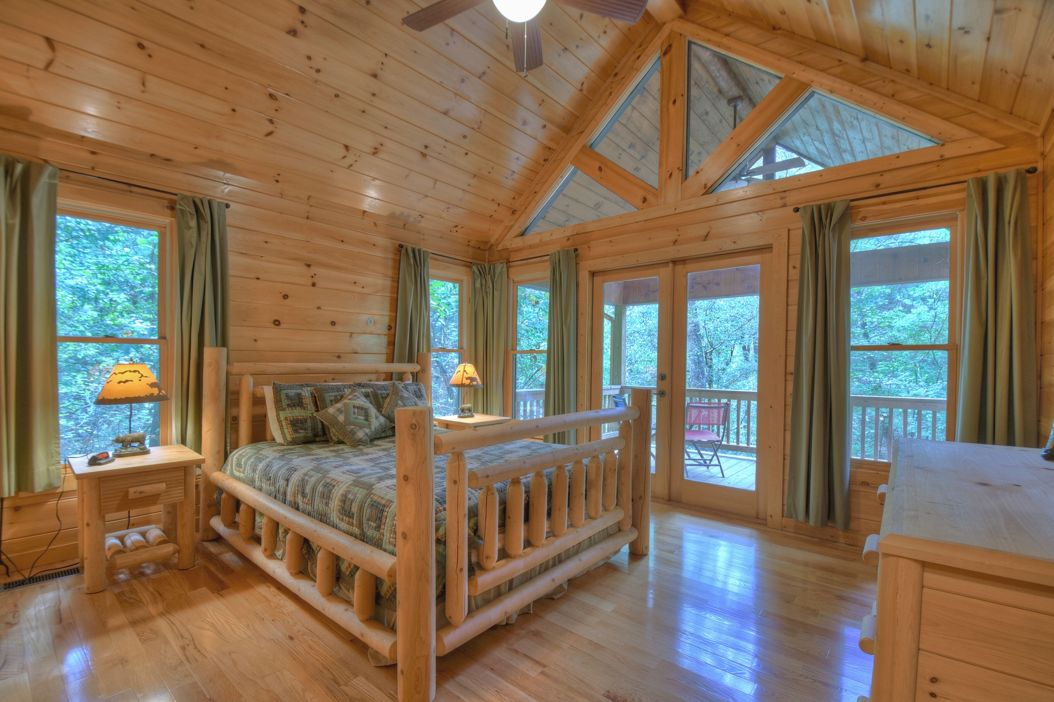 A wooden cabin room with a bed, a desk, and large windows.