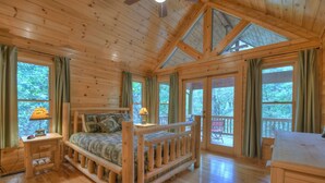 A wooden cabin room with a bed, a desk, and large windows. - Stoney Creek Retreat - Cherry Log, GA (Cherry Log)