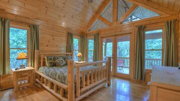 A wooden cabin room with a bed, a desk, and large windows.