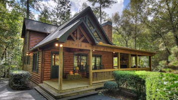 A log cabin with a porch, number 328, surrounded by trees.