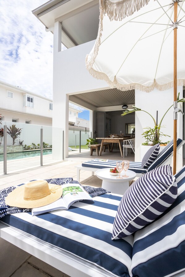 A modern outdoor seating area with striped cushions, a dining table, and a pool in the background.