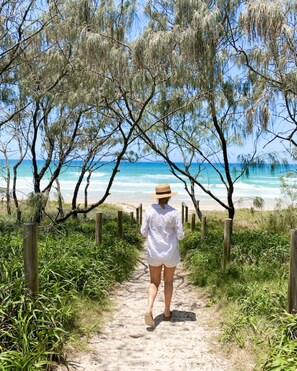 A pathway leading to a beach with a person walking towards the ocean.