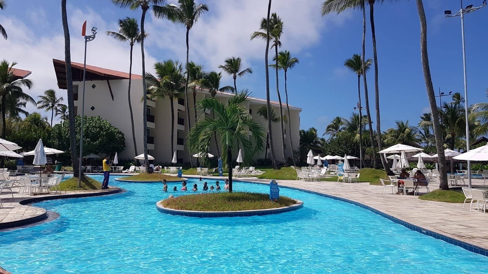 A resort pool area with multiple swimming pools, palm trees, and lounge chairs.
