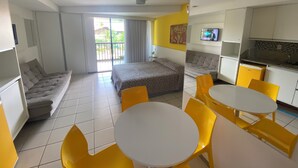 Quarto de hotel moderno com cama, sofá, mesa de jantar com cadeiras, cozinha e varanda com vista.