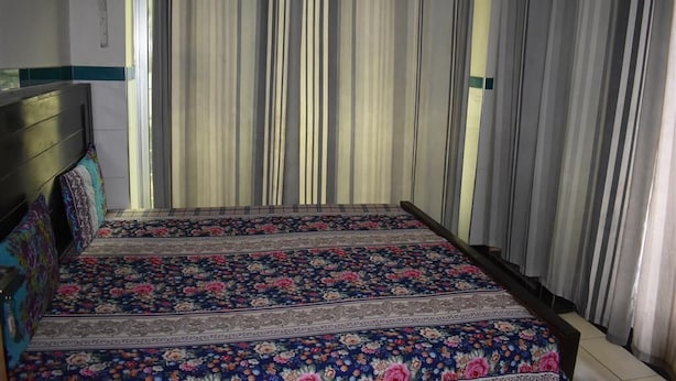 Ein Bett mit floralem Überwurf, Kopfteil und Vorhängen.