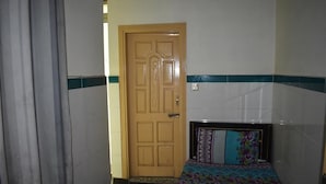 Ein kleines, sauberes Zimmer mit Holztür, einem Bett mit gemusterten Betttextilien und einer gefliesten Wand mit grünem Streifen.